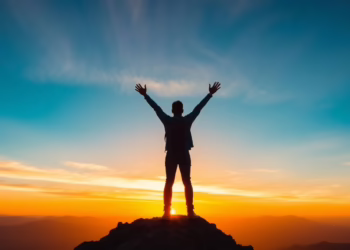 Person on mountain peak, arms raised at sunrise.